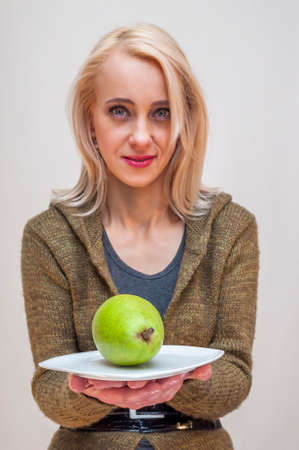 People with fruits and vegetables. Healthy lifestyle. Young woman showing green pear on white plate.の写真素材