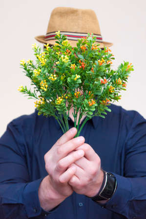 Portrait of young athletic elegant man holding artificial yellow and orange flowers in front of his...