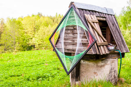 Traditional Lithuanian village with a bit of new waves and style. Old concrete well with wooden roof, metal kettle and psychedelic rhombus decoration on it.の写真素材