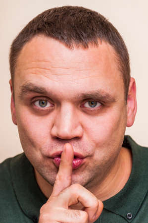 Human face can be different with strong expressions and emotions. Keep silence. Cunning man holding index finger, forefinger on lips.の写真素材