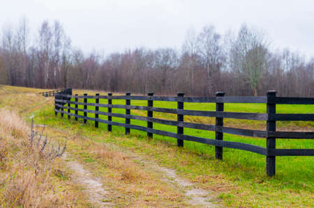 Fall time in country. Here you can see the wooden fence boundary surrounding still green grass field...