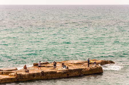 Caesarea, Israel - May 22, 2012: Fishermen fishing on rocky marina on Mediterranean sea near...
