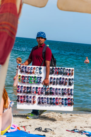 Paralia, Greece - June 14, 2013: Man holding showing offering selling various sunglasses while walking on the beach between resting tourists. Seasonal beach resorts businessesのeditorial素材