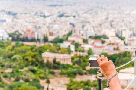 Raised hand arm of tourist holding digital photo camera and taking blind shots of scenic cityscape surroundingsの写真素材