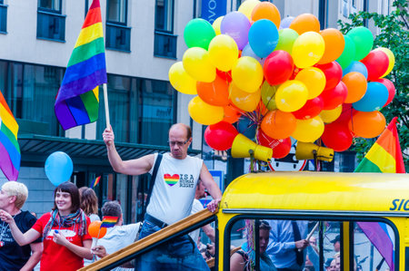 Vilnius, Lithuania - July 27, 2013: Pride parade event in action. Proud man with rainbow flag in his raised arm standing on yellow open top bus decorated with colorful balloons full of demonstratorsのeditorial素材