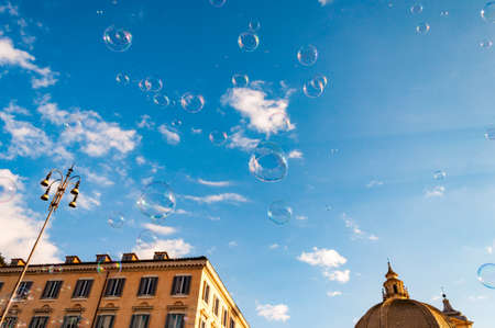 Rome, Italy: Soap bubbles flying on Piazza del Popolo, People Square in Rome surrounded by ancient churches like Santa Maria in Montesanto with its great domes and bell towersの写真素材
