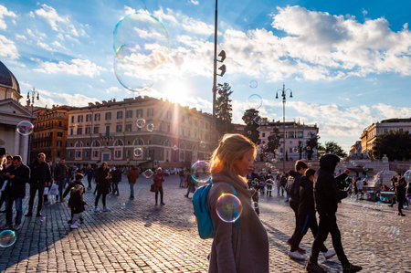 Rome, Italy - November 18, 2018: Kids catching and blowing soap bubbles flying on Piazza del Popolo, People Square in Rome full of people, tourists and locals with Roman architecture on backgroundのeditorial素材