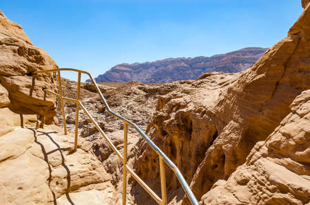 High trails secured by metal railings surrounded by caves, rocks, cliffs of ancient cooper mines canyons and mountains range in Timna National Park in Israelの写真素材