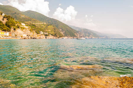 Sea yachts near the rocky coastline, beach and waterfront buildings with green mountains on the...