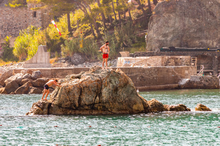 Monterosso Al Mare, Italy - September 02, 2019: A man, tourist with red swimming shorts standing on the rock in Ligurian Sea in Monterosso Al Mare, Cinque Terre, Italyのeditorial素材