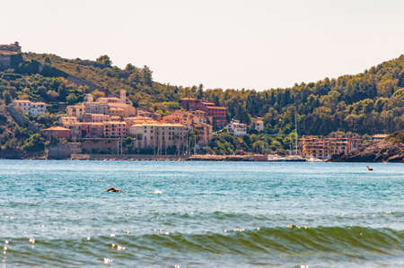 Man swimming in the sea with the landscape cityscape view of the Poggio Pertuso in the front of the...