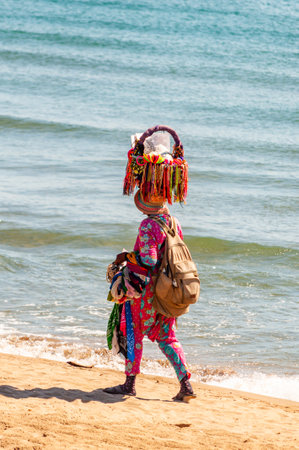 Tenda Gialla, Province of Grosseto, Tuscany, Italy - September 03, 2019: The african woman walking on the beach while holding on her head and the hands various bijouterie, frippery, ornamentals to buyのeditorial素材