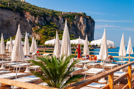 Vico Equense, Naples, Italy - September 05, 2019: People resting on deckchairs under white parasols on wooden terrace in Vico Equensea coastal town near Naples with rocky mountains on the backgroundのeditorial素材