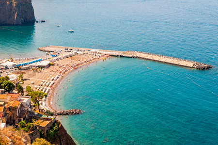 View from above on rocky stones marinas on the beach full of tourists, deckchairs, umbrellas on Tyrrhenian sea bay near Meta and Sorrento cities in Naples region in Italyの写真素材