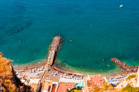 View from above on rocky stones marinas on the beach full of tourists, deckchairs, umbrellas on Tyrrhenian sea bay near Meta and Sorrento cities in Naples region in Italyの写真素材