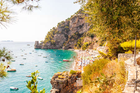 Amazing Positano cityscape on rocky landscape, people on the beach, boats are coming and going to the sea tours, scenic promenade on the edge of rocky mountain surrounded by evergreen trees and plantsの写真素材