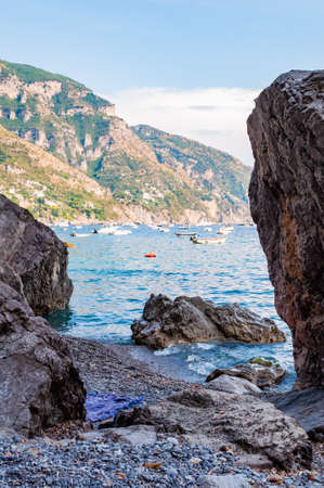 Big boulders lying on the beach, people resting, sunbathing and swimming in Tyrrhenian sea in Positano amazing medieval city on rocky mountains in Campania, Italyの写真素材