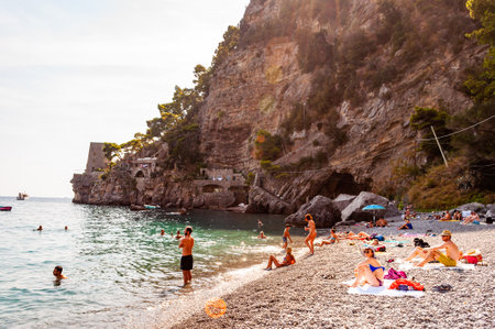 Positano, Italy - September 05, 2019: People resting, sunbathing and swimming on the beautiful pebbles beach of Tyrrhenian sea in Positano, amazing medieval city on rocky mountains in Campania, Italyのeditorial素材