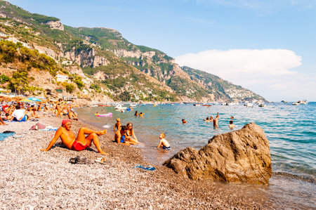 Positano, Italy - September 05, 2019: People resting, sunbathing and swimming on the beautiful pebbles beach of Tyrrhenian sea in Positano, amazing medieval city on rocky mountains in Campania, Italyのeditorial素材