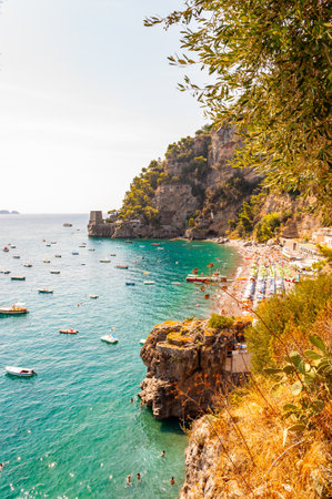 Amazing Positano cityscape on rocky landscape, people on the beach, boats are coming and going to the sea tours, scenic promenade on the edge of rocky mountain surrounded by evergreen trees and plantsのeditorial素材