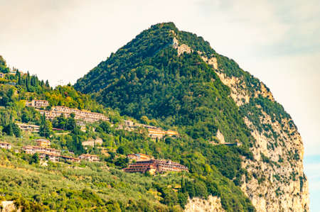 Northern Italian architecture, private houses, hotels and other buildings built high on the rocky mountain on the edge of a cliff. Scenic landscape view on dolomite rocks overgrown with green plantsの写真素材