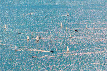 Garda lake, Lombardy, Italy - September 12, 2019: View from above on sailing training. Many sailing boats practice on blue waters of the lake. Group of sportsmen, white sails, strong wind, sunny day.の写真素材