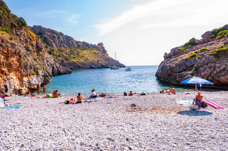 Cala Bianca, Italy - September 06, 2019: Sea yachts floating, people resting on amazing Cala Bianca beach surrounded by rocks of Tyrrhenian sea bay with crystal clear water full of underwater lifeのeditorial素材