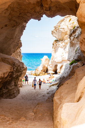 Tropea, Calabria, Italy - September 07, 2019: Amazing seascape view from unique sea cave on famous Rotonda beach. Tourists walking through the grotto, resting on small beach. Tyrrhenian sea landscape.のeditorial素材
