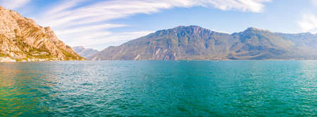 Panorama of beautiful Garda lake in Lombardy, Italy surrounded by high dolomite mountains. Boats and yacht floating on the lake. Various hotels and private houses built on the rocky shores of the lakeの写真素材