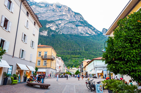 Riva del Garda, Lombardy, Italy - September 12, 2019: Scenic cityscape of Riva del Garda. Cozy city street full of tourists, plants and Italian architecture with high dolomite mountains on backgroundのeditorial素材