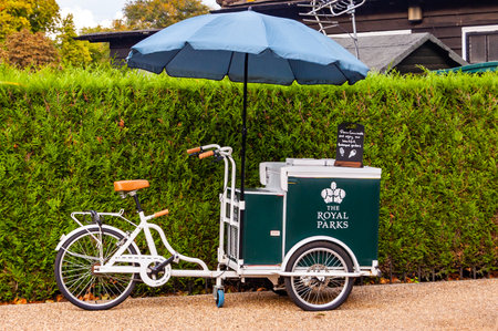 London, United Kingdom - September 15, 2017: Classic ice cream bicycle of the Royal Parks with blue parasol standing near the green natural fenceのeditorial素材