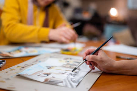 Closeup of watercolor painting process. Brush in hand above painting. Colorful medieval city street on paper board.の写真素材