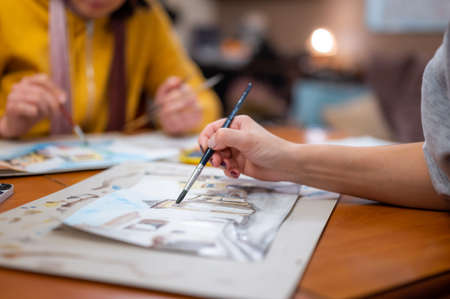 Closeup of watercolor painting process. Brush in hand above painting. Colorful medieval city street on paper board.の写真素材