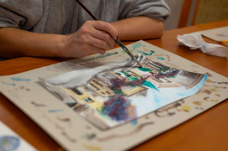 Closeup of vibrant watercolor painting process. Brush in hand above painting. Colorful medieval city street on paper board.の写真素材