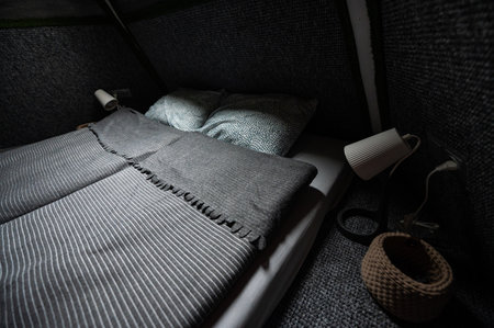 Double bed on carpet floor in bedroom of wooden cabin. Pyramid shape bungalow. Small room, angled...