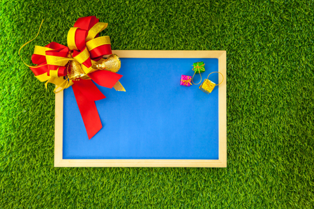 Blue photo frame with ribbon and small colorful box of gift on green grassの写真素材