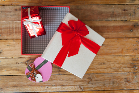 White gift box and red ribbon and mini heart inside on wood background with space.の写真素材