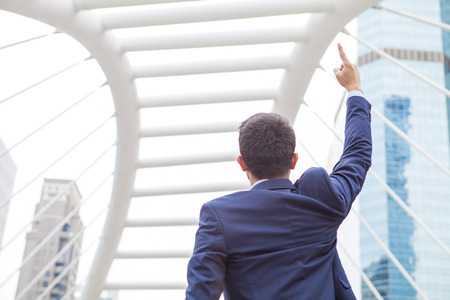 Businessman raising his fist  in the air, with office building background - business success, achievement, and win conceptsの写真素材