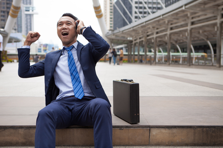 Businessman sitting on stair during callling the phone, with office building background - business success, achievement, and win conceptsの写真素材