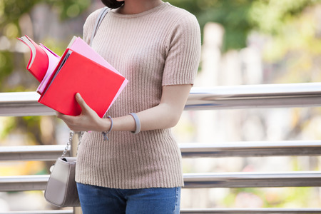 Beautiful Asian female college student holding her books smiling happily standing outdoor, people education learning high school program smart teenager conceptの写真素材