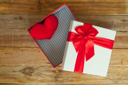 White gift box and red ribbon and mini heart inside on wood background with space.の写真素材