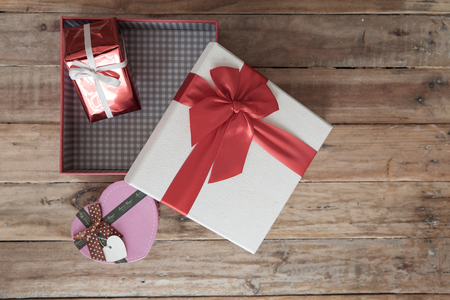 White gift box and red ribbon and mini heart inside on wood background with space.の写真素材