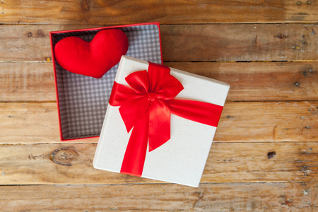 White gift box and red ribbon and mini heart inside on wood background with space.の写真素材
