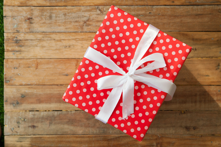 Red gift box and red ribbon and mini heart inside on wood background with space.の写真素材