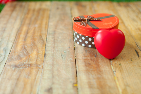 Red gift box and red ribbon and mini heart inside on wood background with space.の写真素材