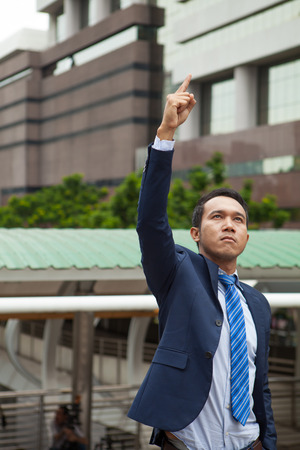 Businessman raising his fist  in the air, with office building background - business success, achievement, and win conceptsの写真素材
