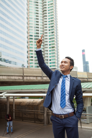 Businessman raising his fist  in the air, with office building background - business success, achievement, and win conceptsの写真素材