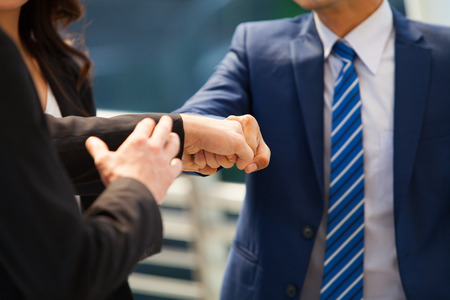 Close up of businessman making a fist bump on building with young woman in background. Business people wear suit do a fist pump together after good deal. Business success and teamwork concept.の写真素材
