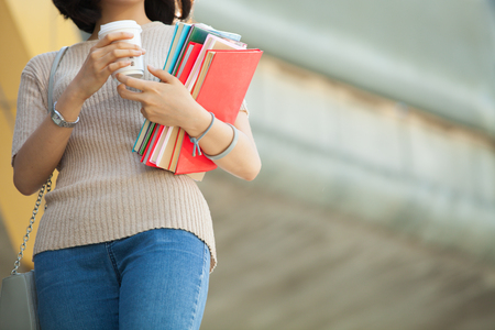 Beautiful Asian female college student holding her books and a cup of coffe standing outdoor, people education learning high school program smart teenager conceptの写真素材