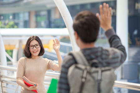 Man and woman students holding many books waving hands say hello to their friendsの写真素材